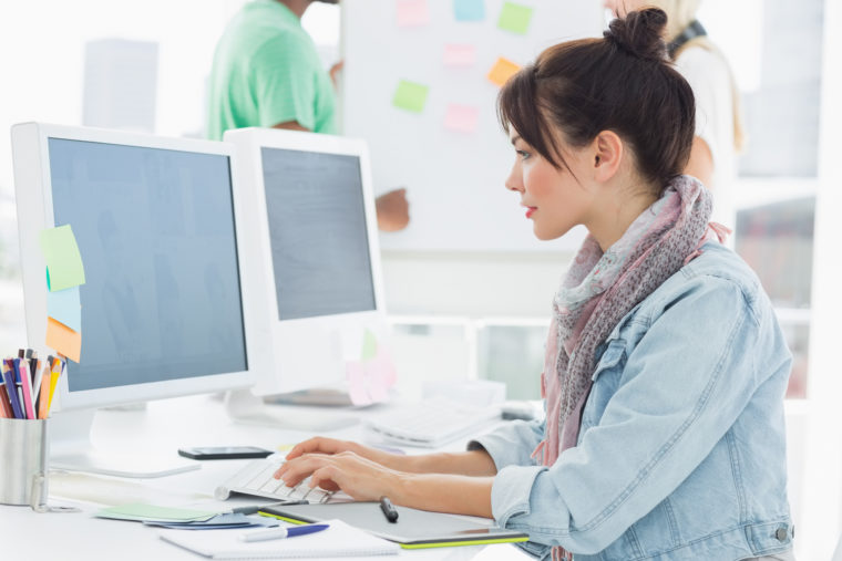 Side view of an artist using computer with colleagues behind at the office