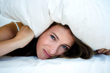 anxious woman hiding under a pillow, lying on her bed
