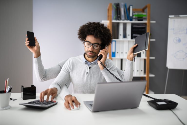 A man sits at a desk multitasking, with three additional arms completing more tasks.