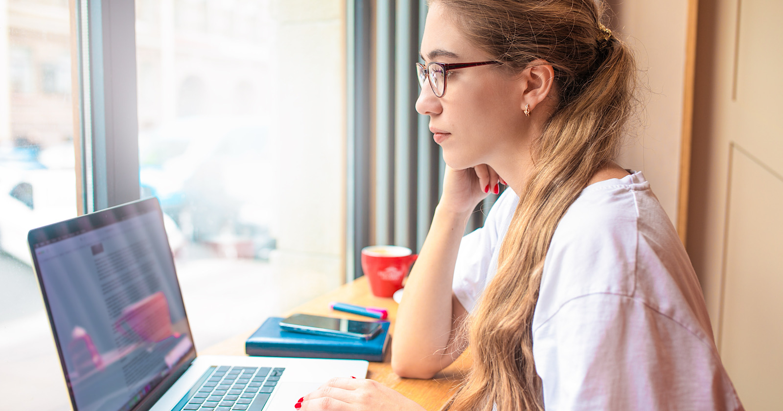 Female in glasses successful business analyst reading newsletter on laptop computer while sitting in coffee shop during recreation time. Woman content writer checking e-mail on notebook gadget