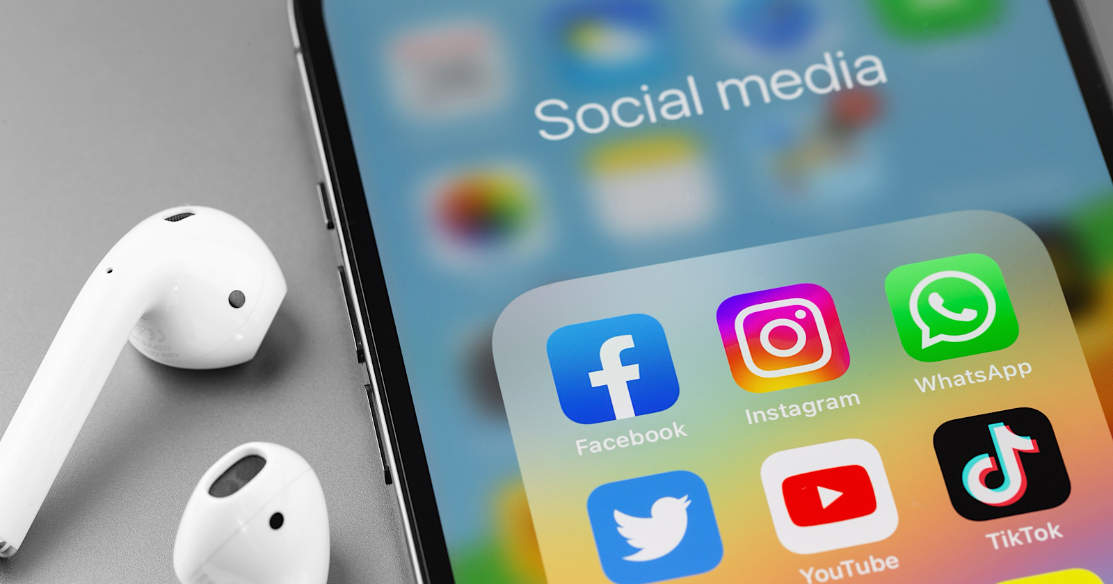 showing social media apps icons of Facebook, Instagram, WhatsApp, Twitter, Youtube, TikTok - on screen smartphone iPhone with AirPods closeup.
