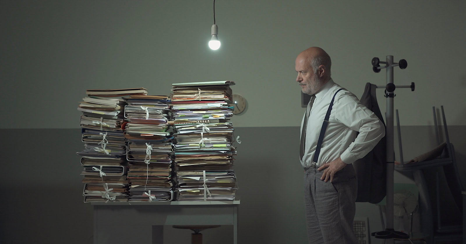 Disappointed stressed businessman staring at the stacked paperwork on his desk